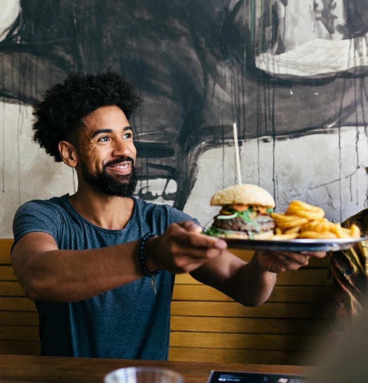 Young man smiling, holding up a plate with a burger and fries on it